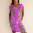 Robe d'été violette à motifs floraux tropicaux, manches courtes, poches latérales, portée par une femme souriante. Mode féminine, style estival.