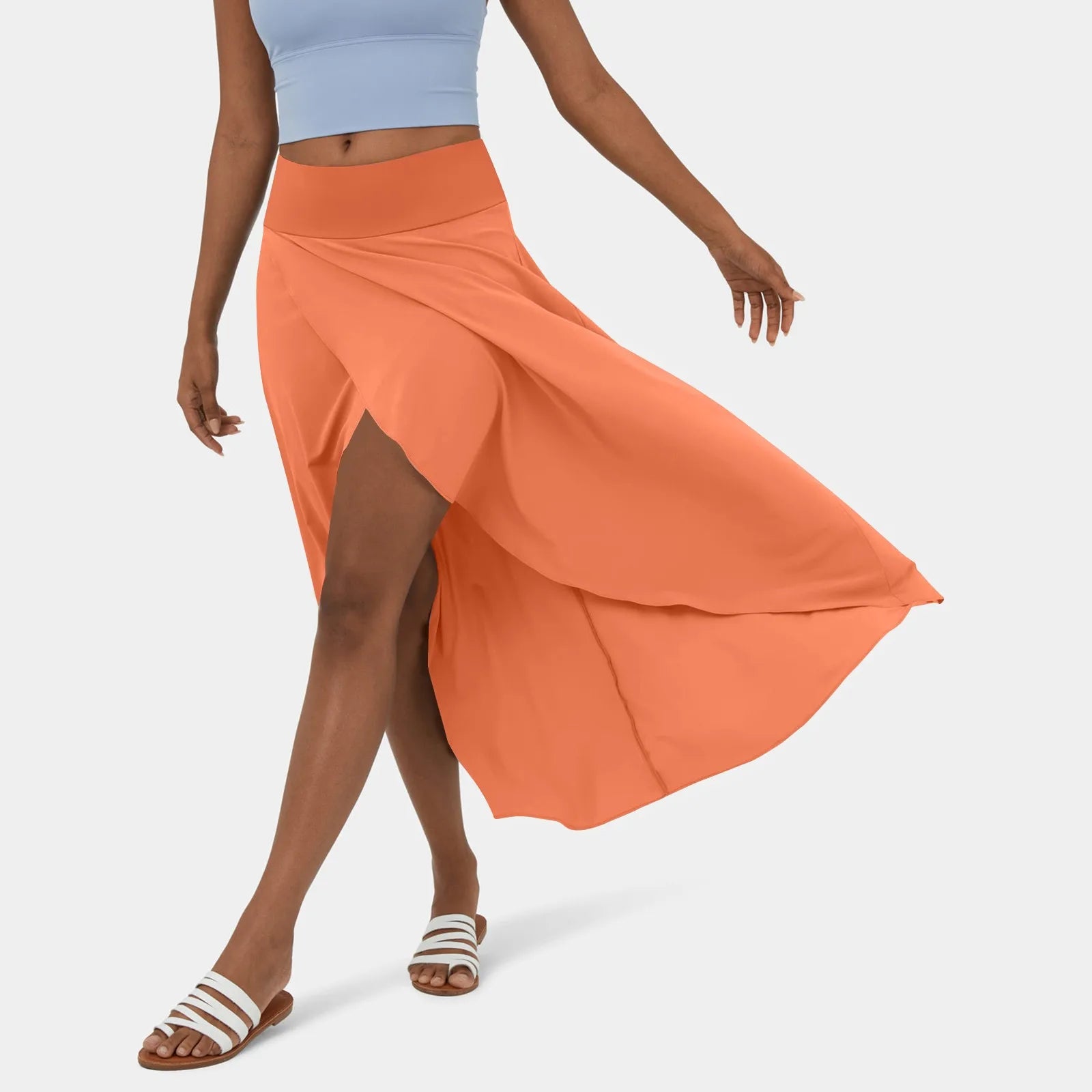 Femme portant une jupe longue orange avec fente, haut bleu clair, sandales blanches. Mode estivale élégante, tenue décontractée chic.