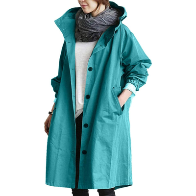 Femme portant un manteau imperméable turquoise avec capuche, écharpe grise, et poches, mode automne-hiver, style décontracté et tendance.