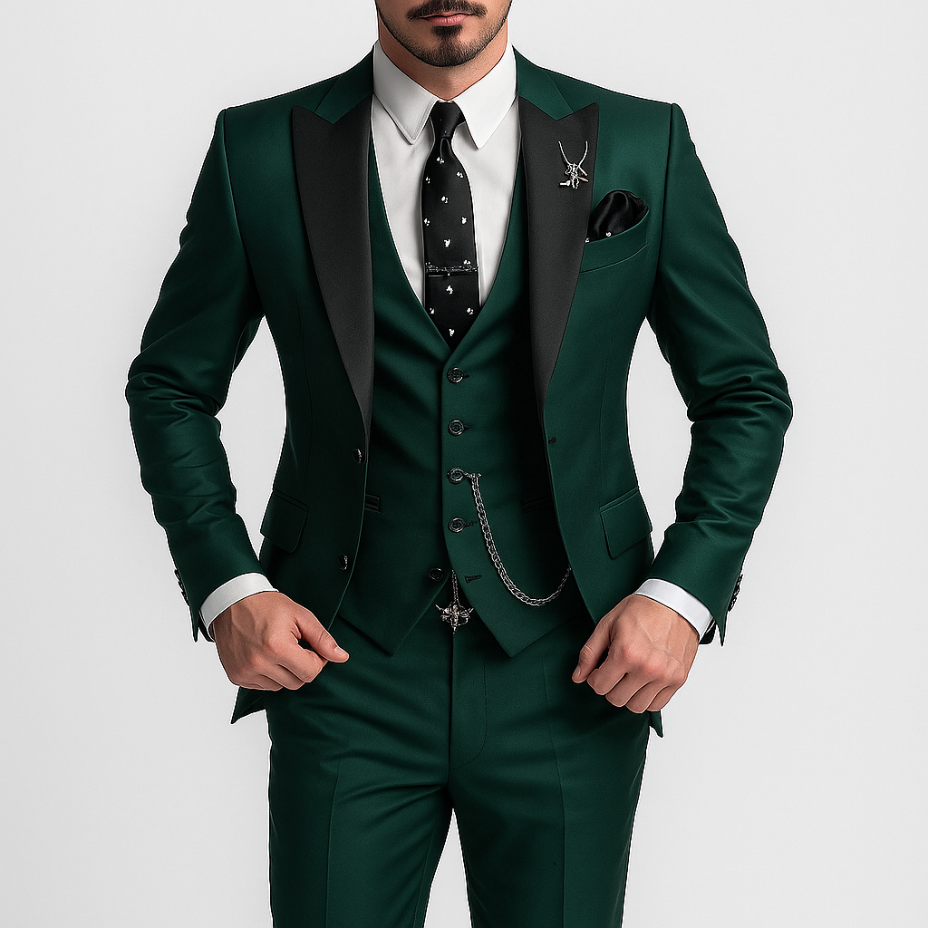 Homme en costume vert élégant avec cravate noire à motifs, gilet assorti et chaîne de montre, posant sur fond blanc. Mode masculine chic.