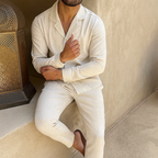 Homme en pyjama beige assis près d'une lanterne en métal, ambiance détente et confort, style décontracté, intérieur moderne.