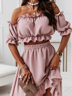 Femme portant une robe rose à épaules dénudées, accessoires dorés, montre élégante et sac à main beige, style chic et tendance.