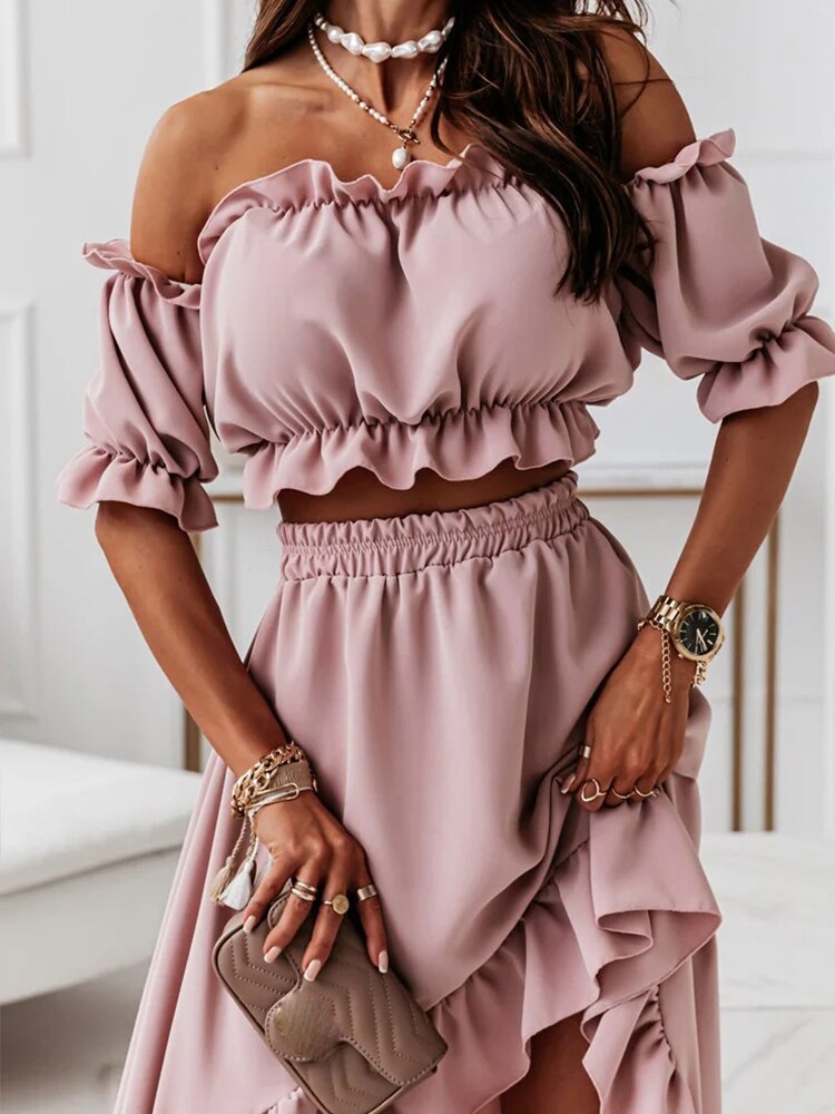 Femme portant une robe rose à épaules dénudées, accessoires dorés, montre élégante et sac à main beige, style chic et tendance.