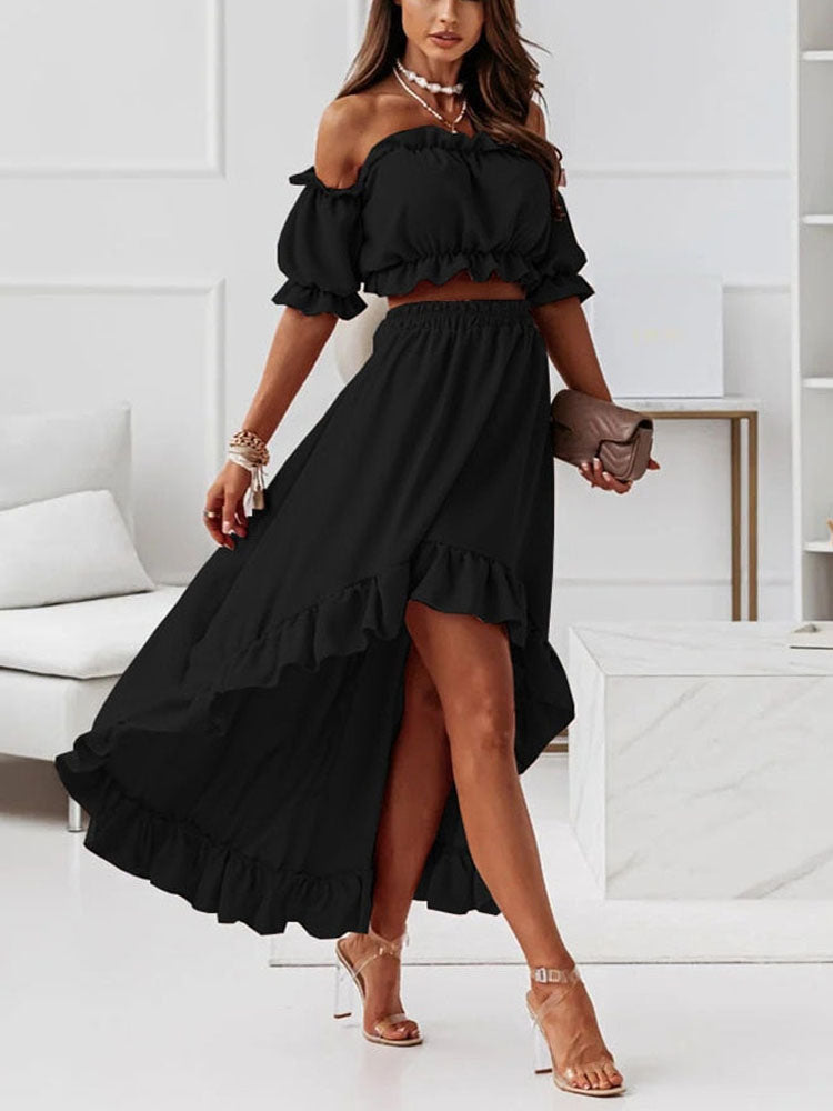 Femme portant une robe noire élégante à épaules dénudées, jupe longue fendue, sandales à talons, dans un salon moderne. Mode chic et tendance.
