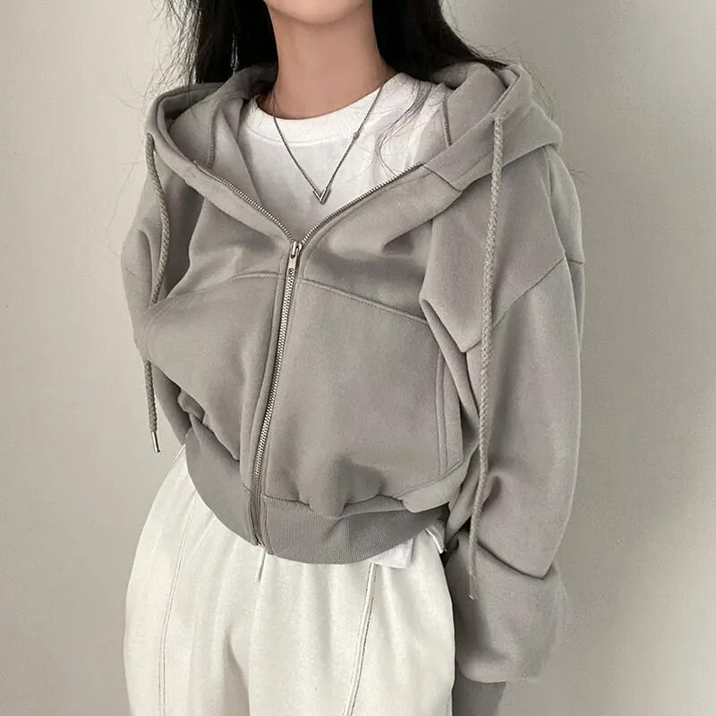 Femme portant un sweat à capuche gris avec fermeture éclair, sur un t-shirt blanc, style décontracté. Mode féminine, vêtements confortables.