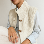 Gilet en laine tricotée crème avec boutons en bois, porté sur une chemise bleue. Mode automne-hiver, style décontracté et élégant.