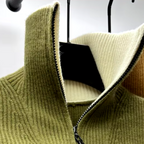 Pull en laine vert olive avec col zippé, exposé sur cintre noir. Mode automne-hiver, vêtement chaud et élégant, texture côtelée.