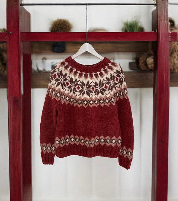 Pull-over rouge en laine avec motif nordique suspendu sur un cintre en bois. Tricot chaud, style scandinave, idéal pour l'hiver.