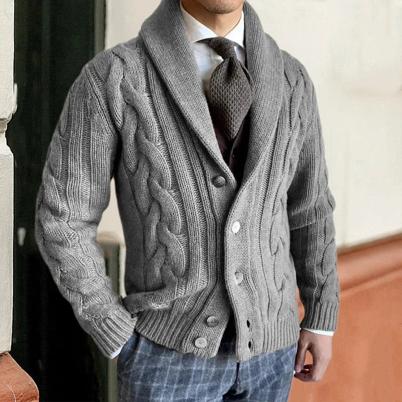 Homme portant un cardigan gris en maille torsadée, élégant et chaud, avec chemise blanche et cravate marron, mode automne-hiver chic.