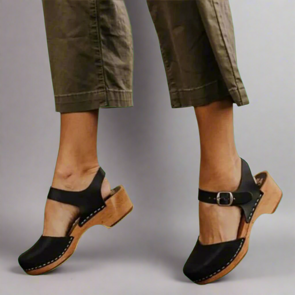 Chaussures à talons en bois noir avec bride, portées avec un pantalon kaki. Mode féminine, style rétro, confort et élégance.