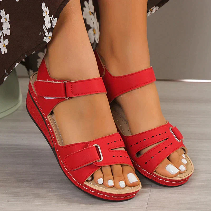 Sandales rouges pour femmes avec brides ajustables, design confortable, portées sur un sol en bois, robe à fleurs visible. Mode estivale élégante.