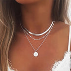 Collier femme en argent superposé, avec pendentif rond et chaînes délicates, porté sur peau bronzée. Accessoire mode tendance et élégant.