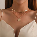 Collier femme en or à trois rangs avec pendentif soleil, porté sur une robe blanche. Bijoux élégants, mode féminine, accessoires tendance.