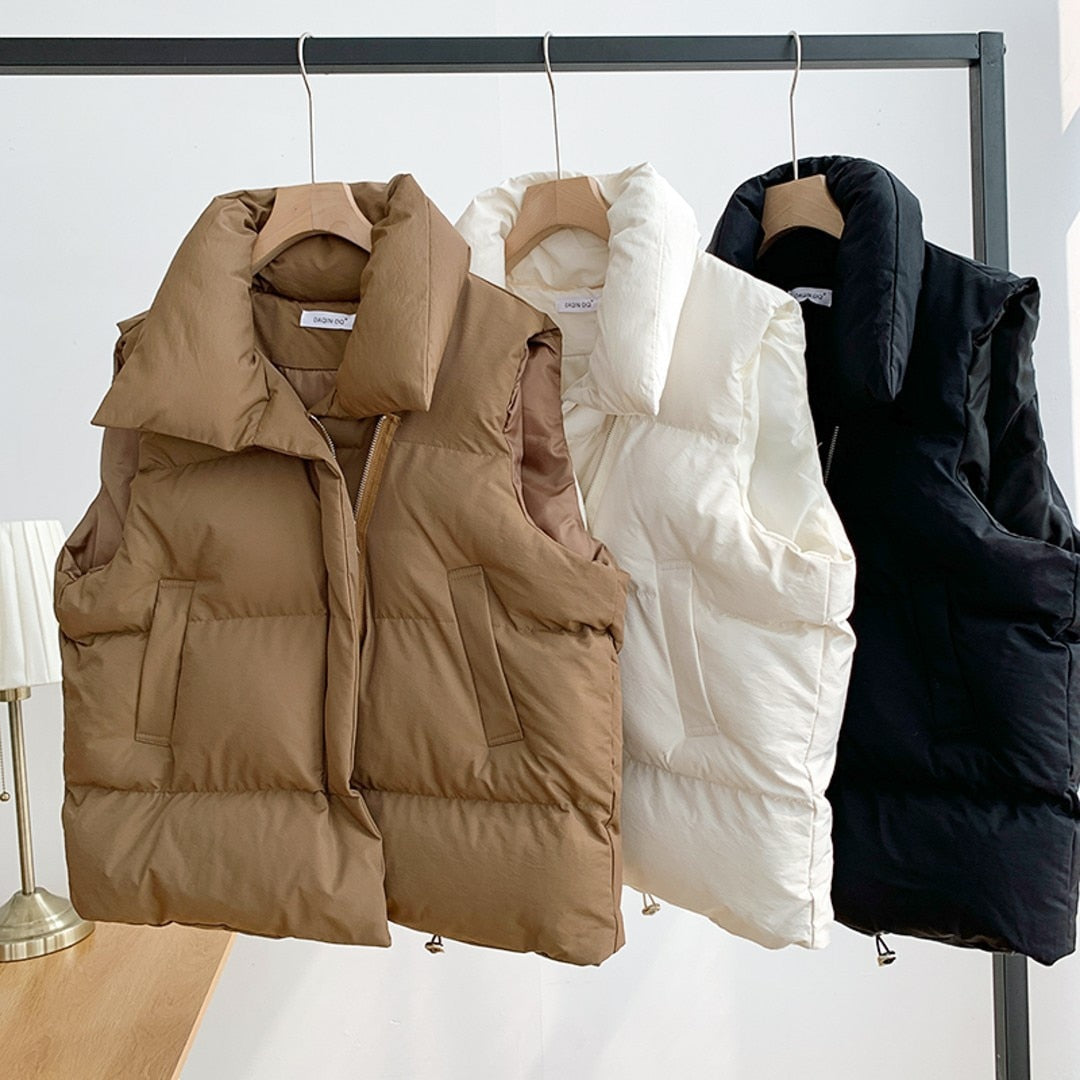 Trois doudounes sans manches suspendues : marron, blanche et noire. Mode hiver, vêtements chauds, vestes matelassées pour femmes.