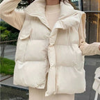 Femme portant une doudoune sans manches beige, tendance automne-hiver, devant un décor urbain moderne. Mode féminine, vêtement chaud et élégant.