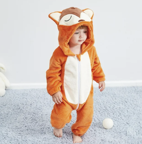 Enfant portant une grenouillère renard en peluche orange, debout sur un tapis bleu avec une balle blanche à proximité. Pyjama animalier mignon.