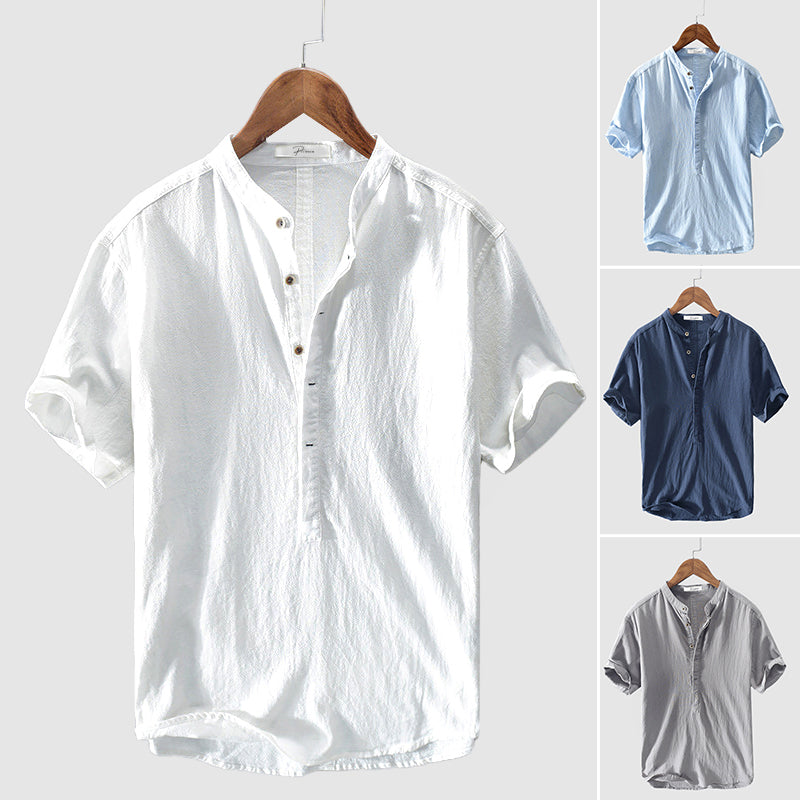 Chemise en lin pour homme, col mao, manches courtes, disponible en blanc, bleu clair, bleu foncé et gris, suspendue sur cintre en bois.