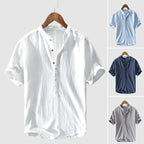 Chemise en lin pour homme, col mao, manches courtes, disponible en blanc, bleu clair, bleu foncé et gris, suspendue sur cintre en bois.