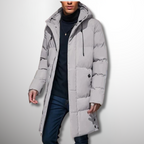 Homme portant un manteau d'hiver gris clair avec capuche, fermeture éclair et poches, sur fond blanc. Mode masculine, vêtement chaud, style moderne.