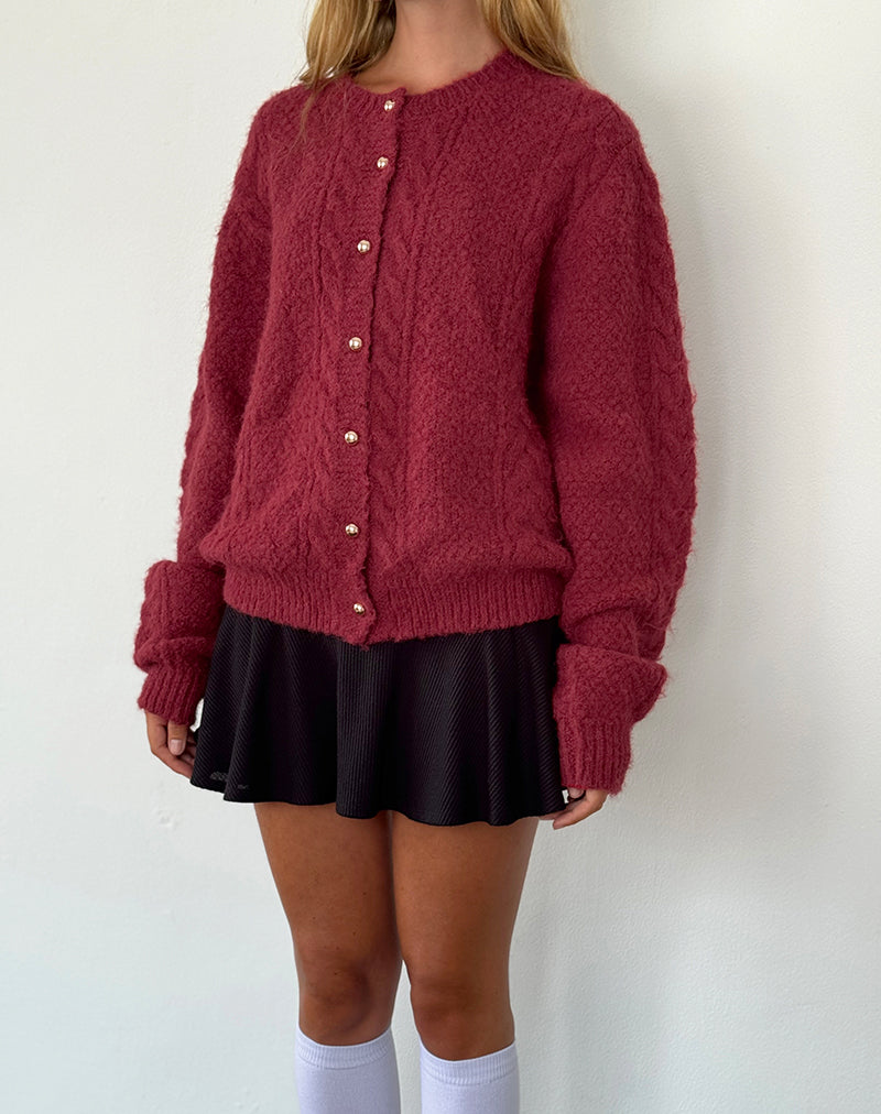Femme portant un cardigan rouge texturé avec boutons dorés, jupe noire plissée et chaussettes blanches. Mode automne-hiver, style décontracté.