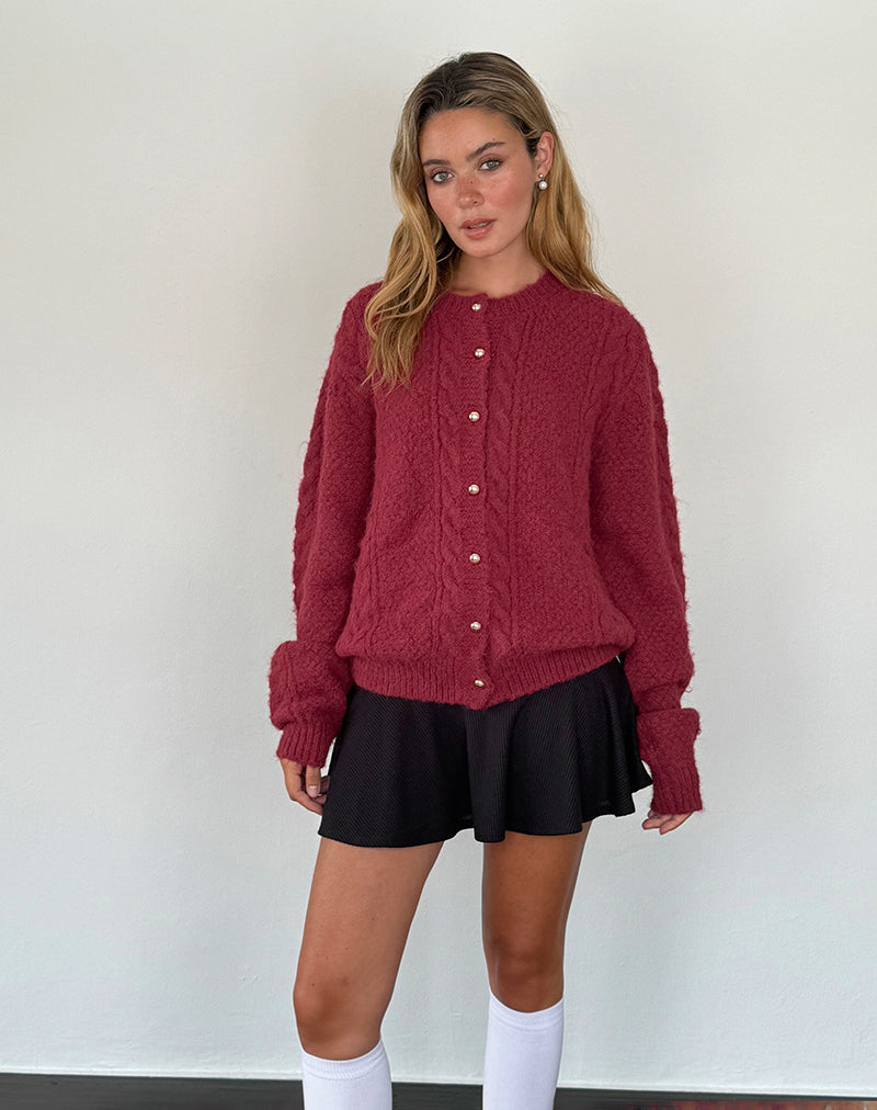 Jeune femme portant un cardigan rouge texturé avec boutons, jupe noire et chaussettes blanches. Mode automne-hiver, style décontracté et élégant.