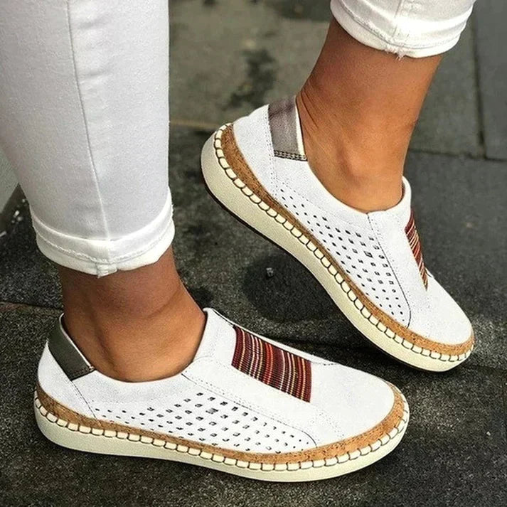 Chaussures blanches décontractées pour femmes avec motifs colorés, semelle en liège, portées avec un pantalon blanc. Mode estivale, confort, style urbain.