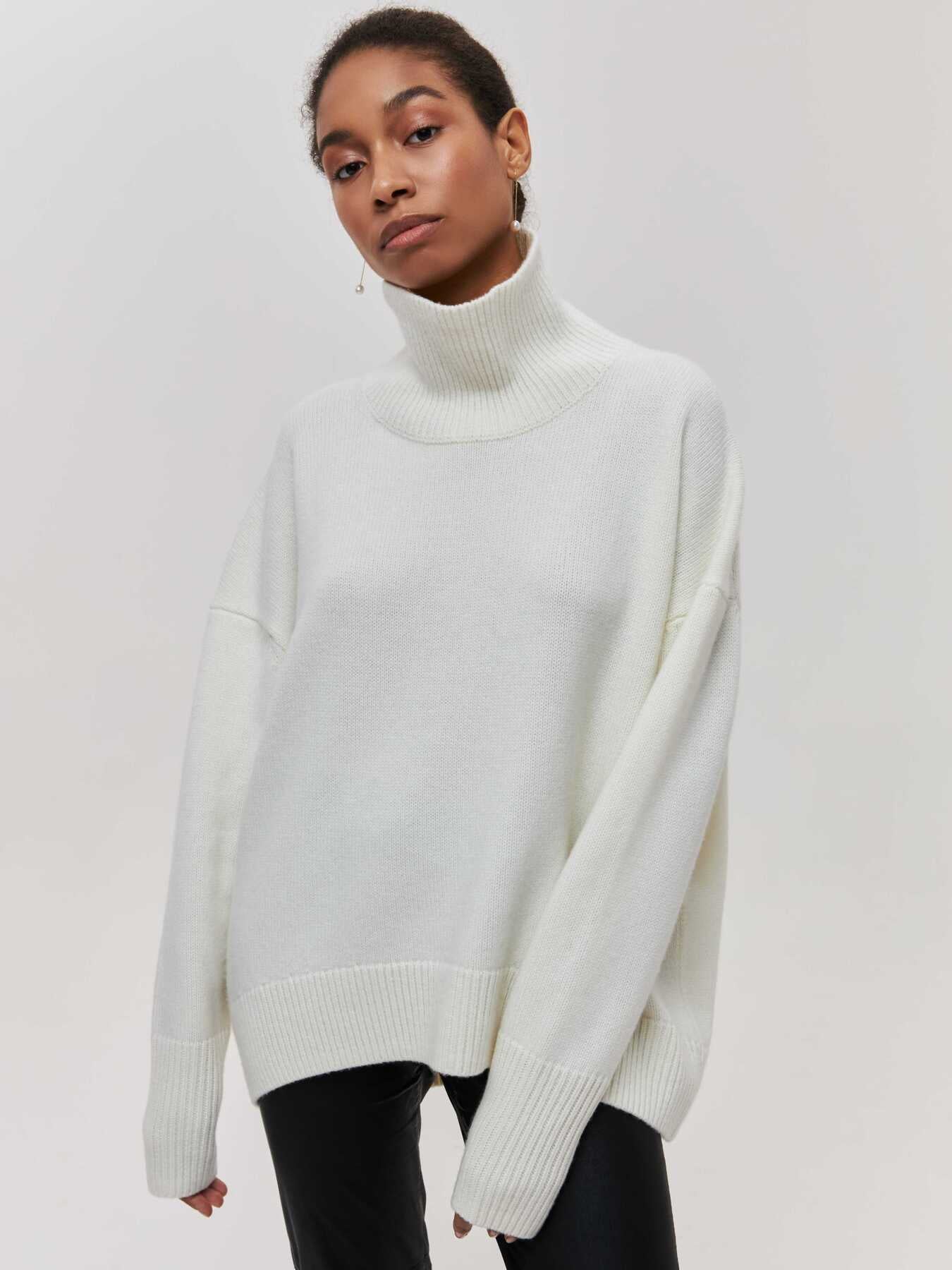 Femme portant un pull blanc à col roulé, manches longues, style décontracté, sur fond neutre. Mode automne-hiver, tendance minimaliste.
