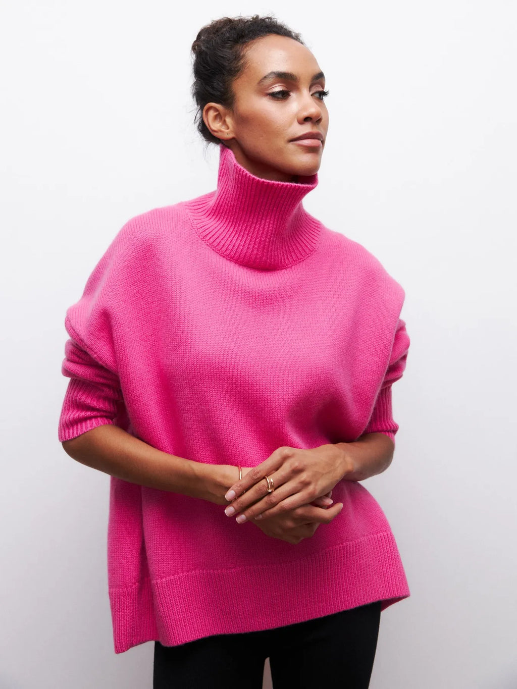 Femme portant un pull rose à col roulé, manches longues, posant contre un fond blanc. Mode automne, style décontracté, tendance féminine.