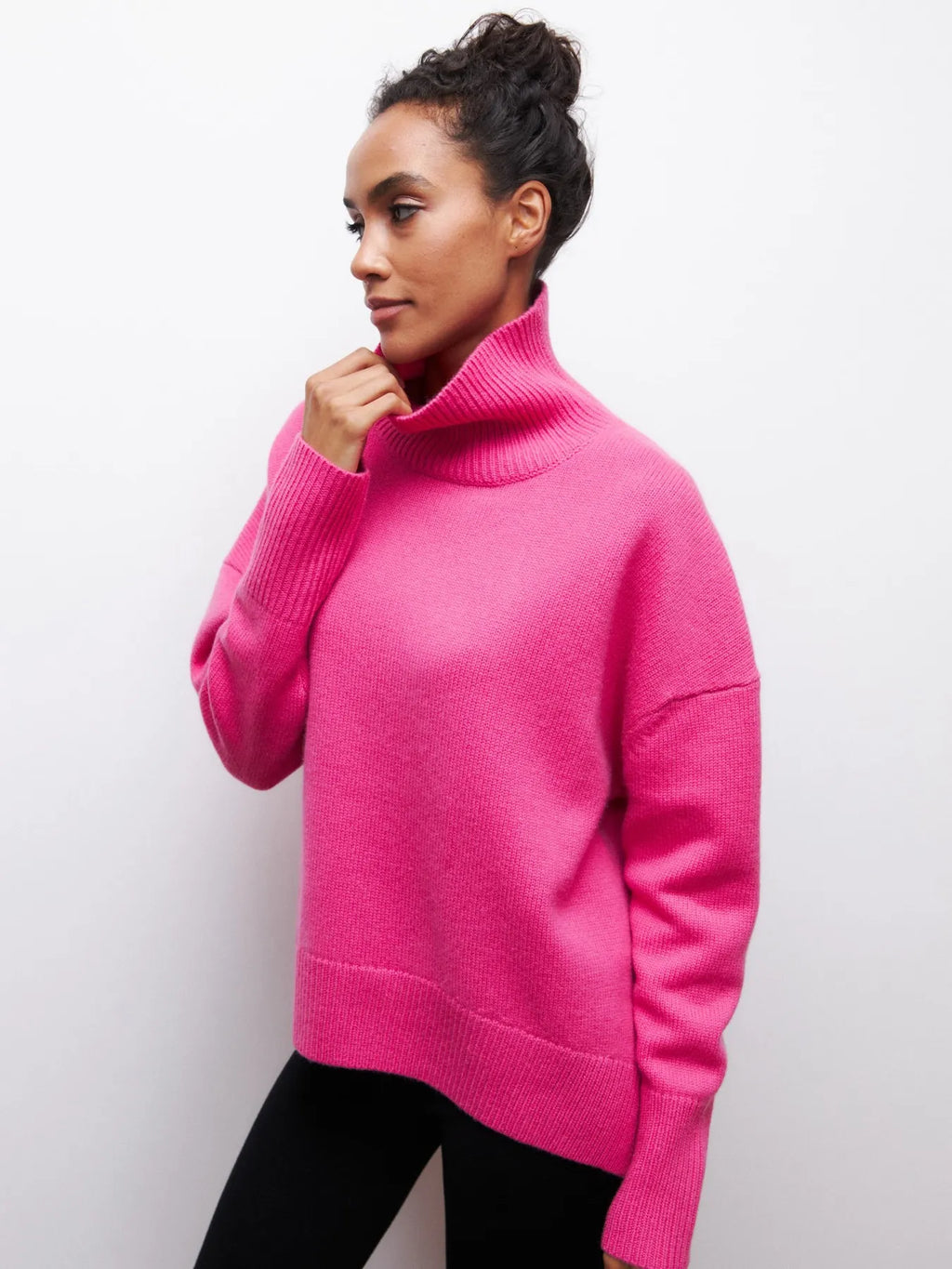 Femme portant un pull rose à col roulé, manches longues, sur fond blanc. Mode féminine, style décontracté, tendance automne-hiver.