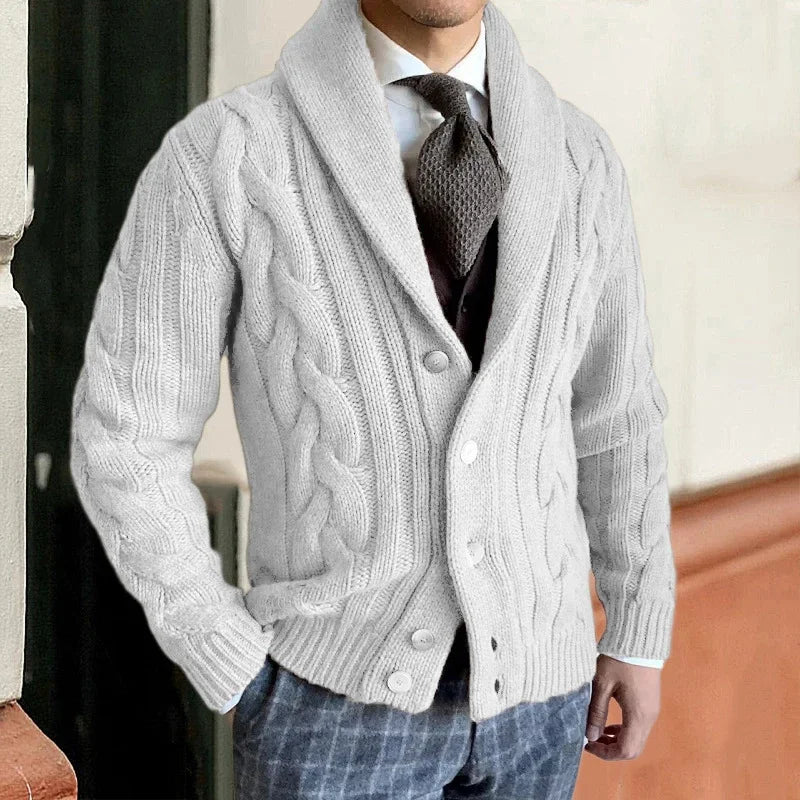 Homme portant un cardigan en maille torsadée gris, élégant et chic, avec cravate et pantalon à carreaux. Mode masculine automne-hiver tendance.