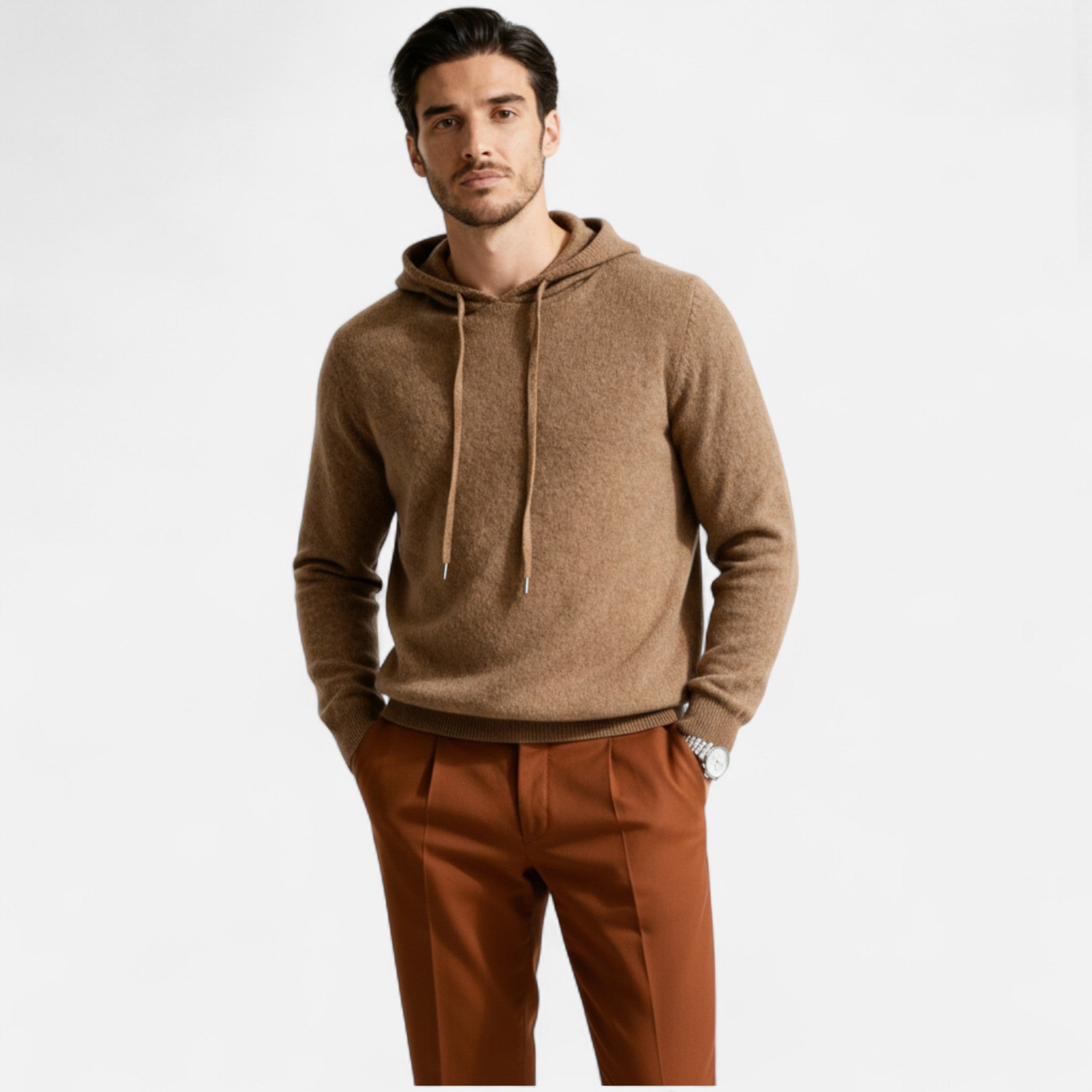 Homme portant un pull à capuche marron et un pantalon orange, posant sur fond blanc. Mode masculine élégante, tenue automne-hiver tendance.