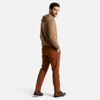 Homme portant un pull à capuche beige et un pantalon marron, regardant en arrière. Mode masculine élégante, tenue automne-hiver, style décontracté.