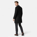 Homme en manteau noir élégant, pantalon gris, chaussures marron, pose de dos. Mode masculine, style automne-hiver, tenue chic et moderne.