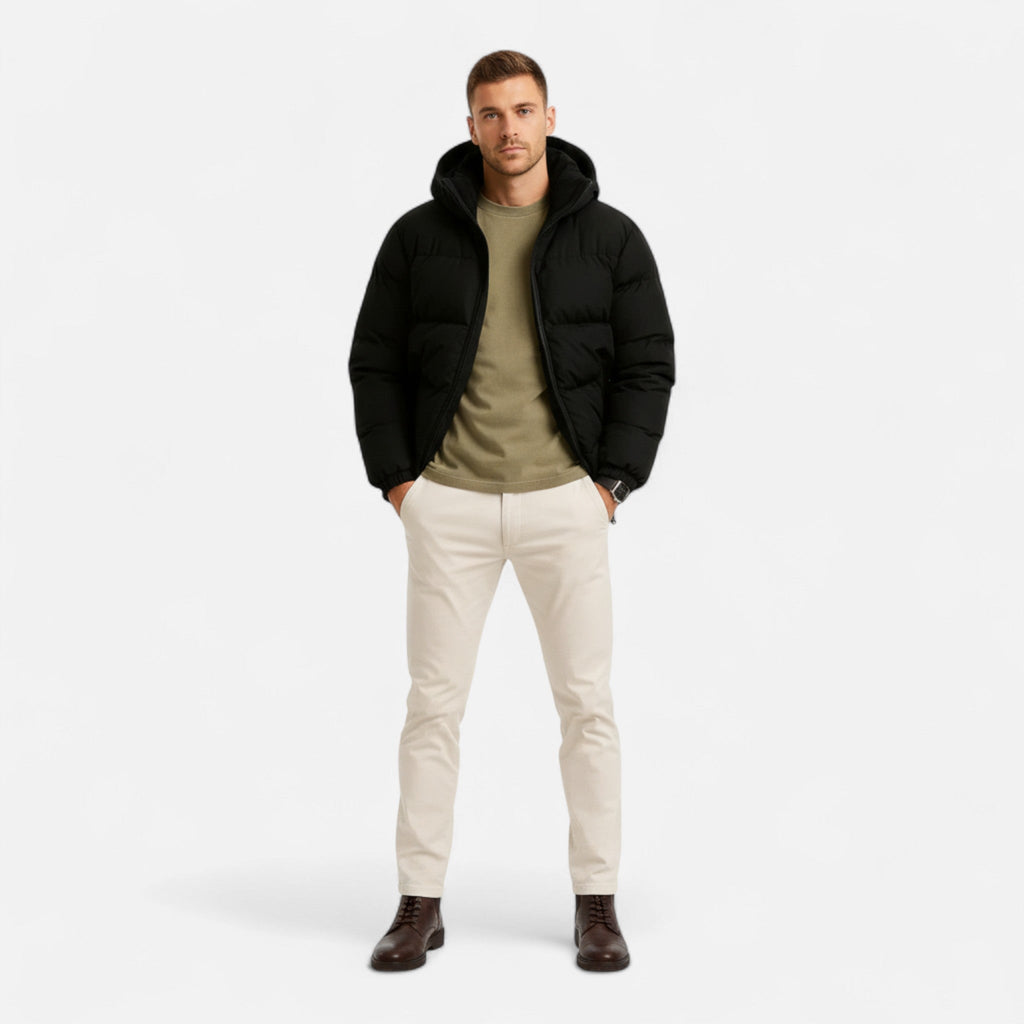 Homme portant une doudoune noire, pull kaki, pantalon beige et bottes marron. Mode masculine hiver, tenue décontractée élégante.