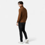 Homme portant un pull marron à col roulé, jeans noirs et baskets blanches, regardant en arrière. Mode masculine automne-hiver, style décontracté.