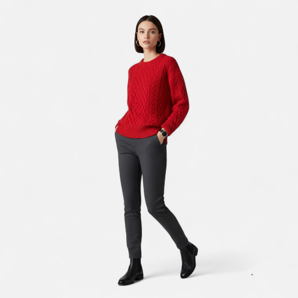 Femme portant un pull rouge en maille torsadée, pantalon gris et bottines noires. Mode automne-hiver, tenue élégante et décontractée.