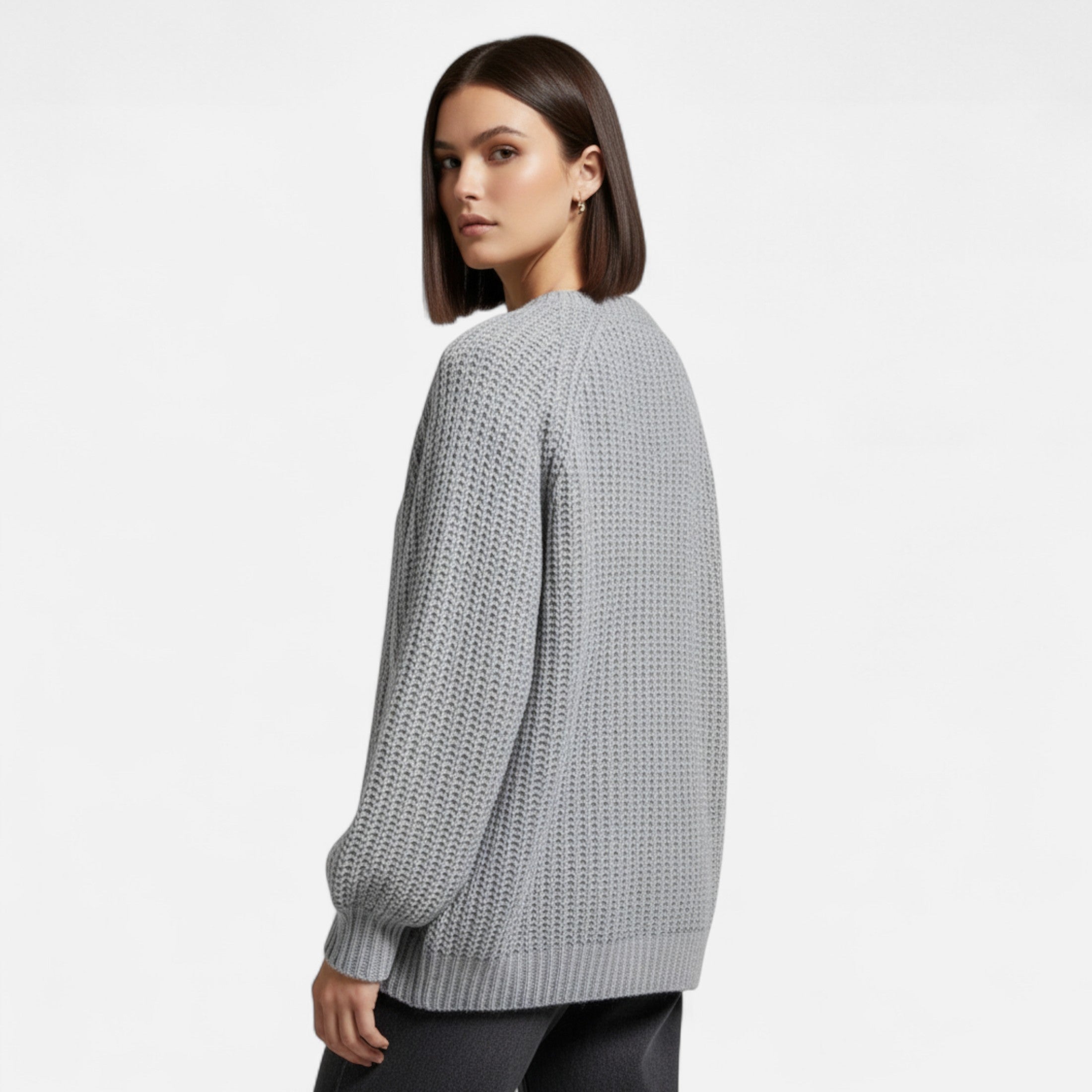 Femme portant un pull gris en maille texturée, manches longues, coupe décontractée, sur fond blanc. Mode automne-hiver, style élégant et moderne.