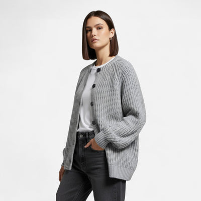 Femme portant un cardigan gris en maille avec boutons, sur un t-shirt blanc et un jean gris. Mode automne-hiver, style décontracté et élégant.