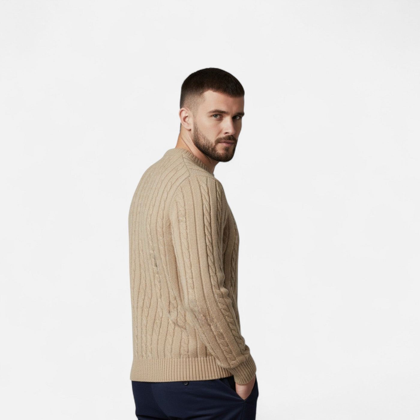 Homme portant un pull en laine beige torsadé, manches longues, sur fond blanc. Mode masculine élégante, style automne-hiver, confort et chaleur.