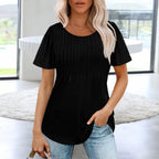 Femme portant un t-shirt noir élégant avec des manches courtes, debout dans un intérieur moderne. Mode féminine, style décontracté, tendance actuelle.