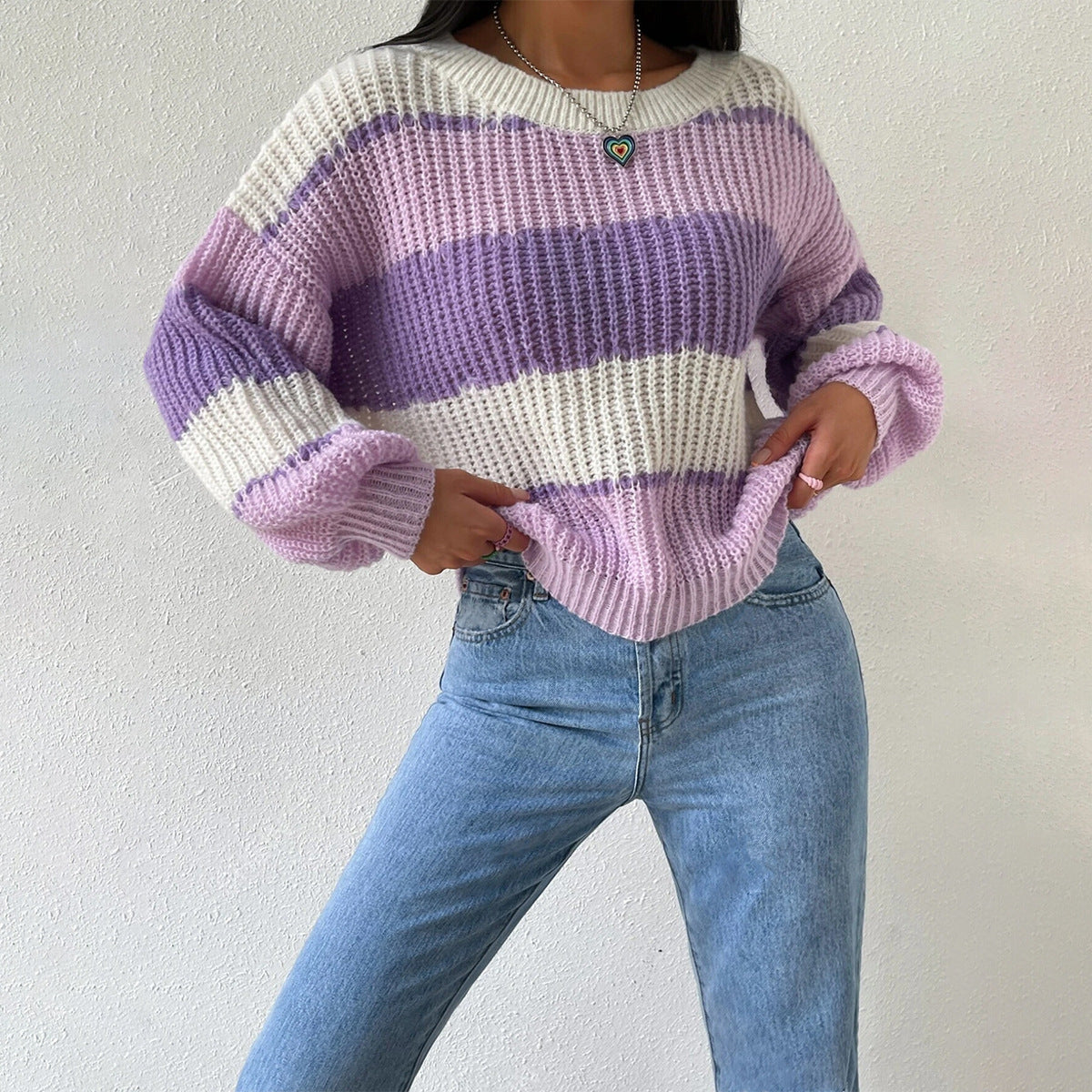 Femme portant un pull rayé violet et blanc, en maille épaisse, avec un jean bleu clair. Mode automne-hiver, style décontracté et tendance.