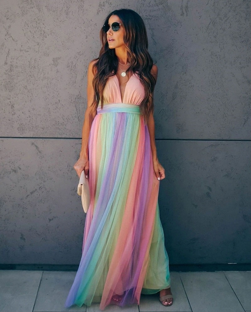 Robe longue multicolore en tulle, décolleté plongeant, portée par une femme avec lunettes de soleil, devant un mur gris. Mode élégante et estivale.