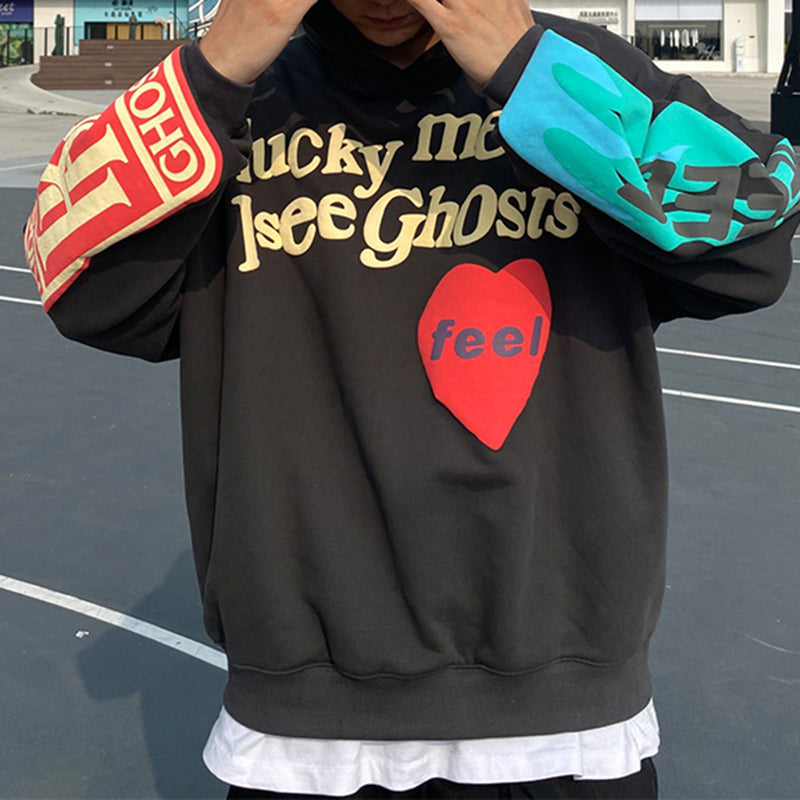 Sweat à capuche noir avec texte "Lucky Me I See Ghosts", cœur rouge "feel", manches colorées. Mode urbaine, streetwear tendance, style décontracté.