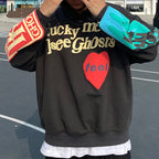Sweat à capuche noir avec texte "Lucky Me I See Ghosts", cœur rouge "feel", manches colorées. Mode urbaine, streetwear tendance, style décontracté.