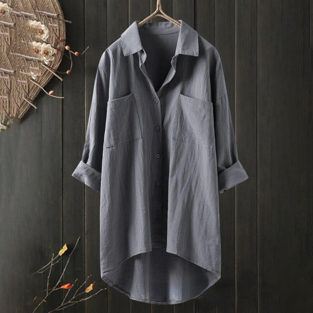 Chemise grise en lin suspendue, manches longues, col classique, boutons, poches avant, fond bois sombre, style décontracté, mode automne.