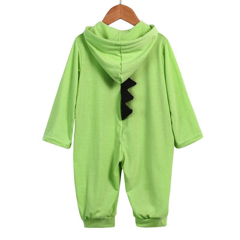 Combinaison bébé verte en forme de dinosaure avec capuche et crête noire, suspendue sur un cintre en bois. Vêtement enfant confortable et ludique.
