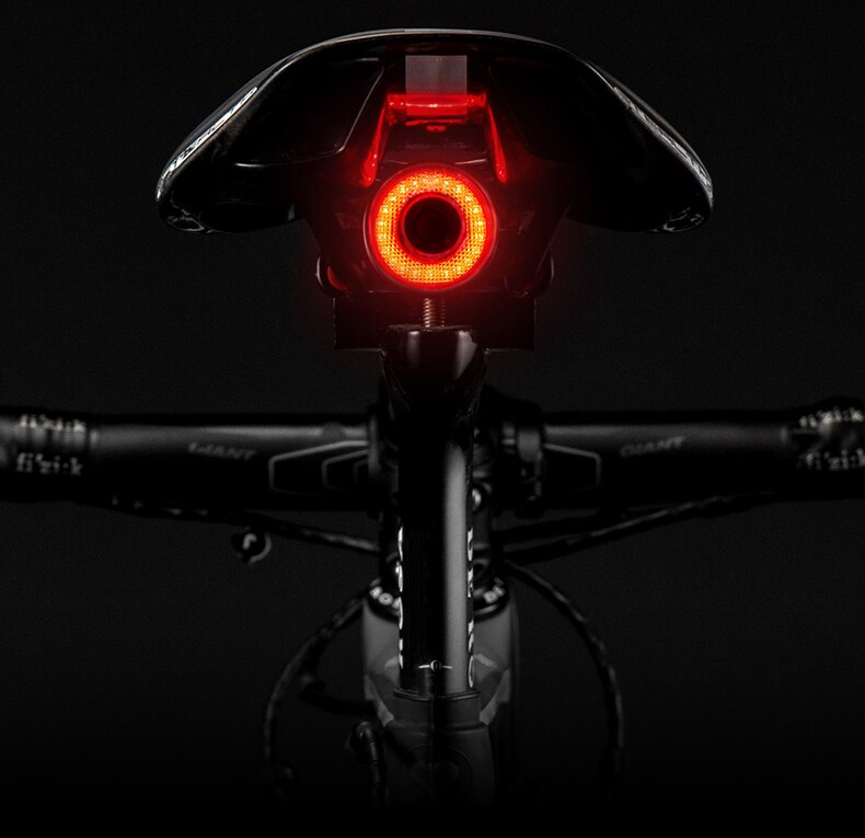 Vélo avec feu arrière LED rouge allumé, selle noire, guidon visible, sur fond noir. Éclairage vélo, sécurité nocturne, accessoire cyclisme.