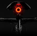 Vélo avec feu arrière LED rouge allumé, selle noire, guidon visible, sur fond noir. Éclairage vélo, sécurité nocturne, accessoire cyclisme.