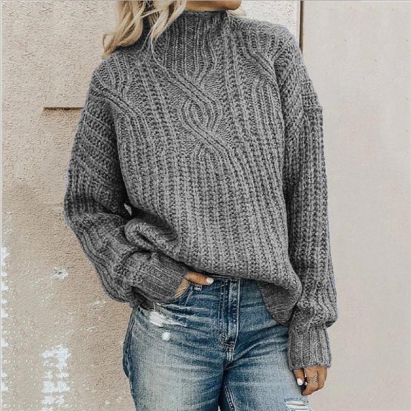 Femme portant un pull en laine gris à col roulé, manches longues, avec un motif torsadé, associée à un jean décontracté. Mode automne-hiver tendance.