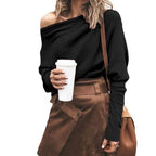 Femme en pull noir à épaules dénudées, jupe marron, tenant un gobelet de café blanc, sac en bandoulière. Mode automne chic et décontractée.